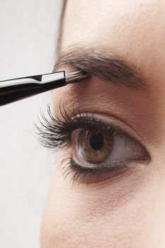 woman applying eye make-up with brush on white background