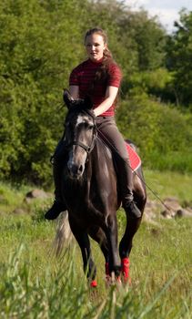 Girl astride a horse galloping on a background of green wood