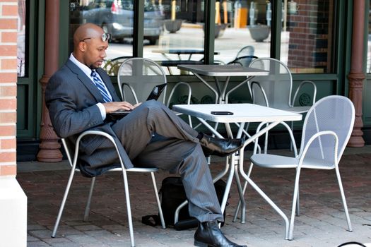 An African American business man in his early 30s using his laptop or netbook computer while seated at a cafe table outdoors.