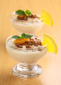 Delicious homemade rice pudding with cinnamon garnished with orange peel and mint leaf and a slice of orange on the rim of the bowl (Selective Focus, Focus on the orange peel and the mint leaf as well as the orange slice on the rim of the first dessert)