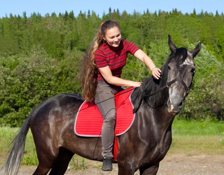 A girl with her hair stroked the horse against the backdrop of green forest