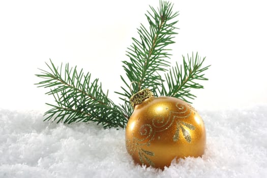 one golden Christmas ball with pine branches lies in the snow