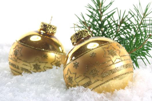 two golden Christmas balls with pine branches lying in the snow