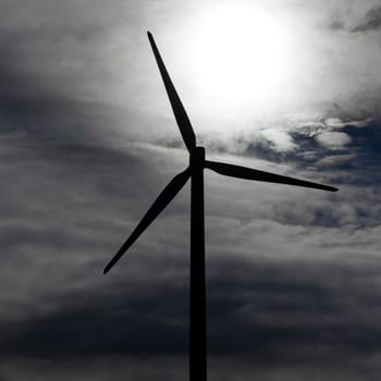 Silhouette of green energy producing large wind turbine against cloudy and windy sky.