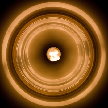 Abstract of lighted energy saving flourescent lightbulb in center of reflective lamp shade.