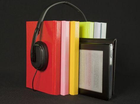 Audiobooks concept -  Colorful books with headphones and electronic book reader on black background
