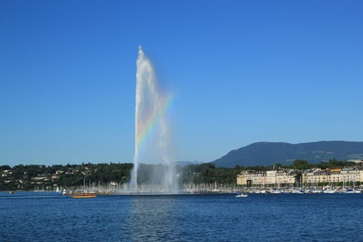 View of Geneva city, Switzerland. A beautiful rainbow colors the mist on the 140 m water fountain on Geneva Lake. It is the symbol of this swiss city and is called the Jet D'eau.