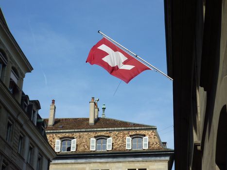 Swiss flag hanging on a building in the old town of Geneva, Switzerland, by beautiful weather