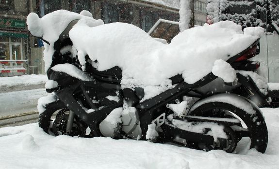 Big black motorbike covered with snow by winter weather in a street of Geneva, Switzerland