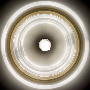 Abstract of lighted energy saving flourescent lightbulb in center of reflective lamp shade.