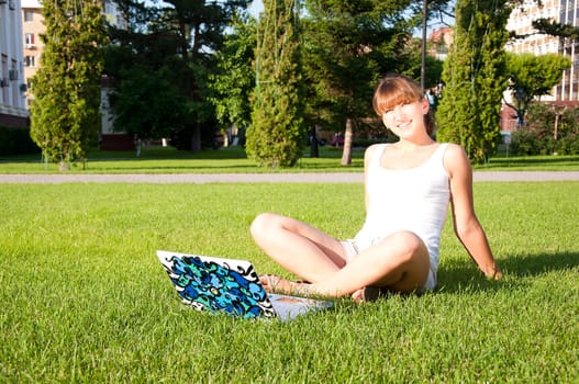 young girl sitting in the park with your laptop, green grass backgrounf