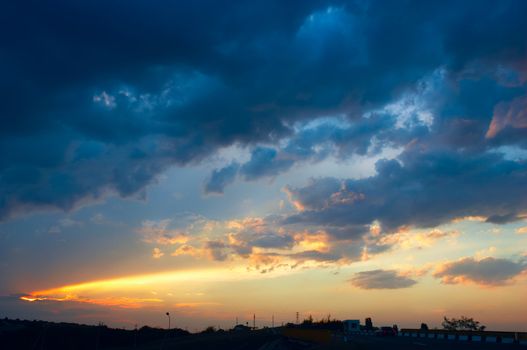 colorful sunset with clouds and sunbeams over rural skyline