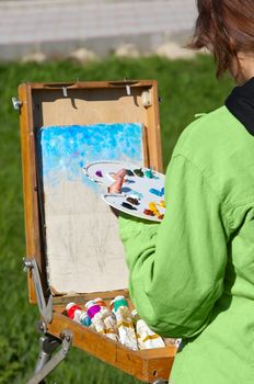 young female artist working at open air, creating oil paint. selective focus.