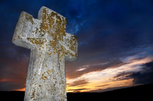 brightly lit stone cross on the sunset background