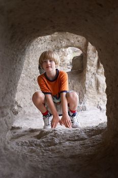 smiling boy sitting behind the stone tunnel