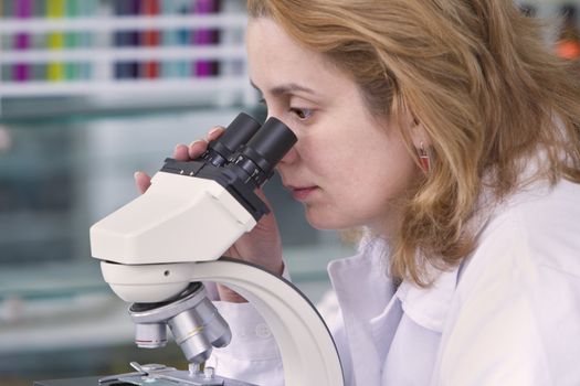 Female researcher looking through a microscope in a laboratory.