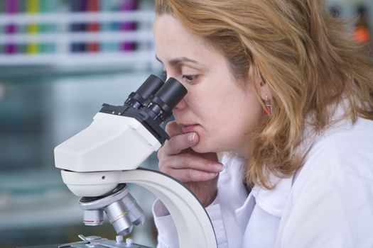 Female researcher looking through a microscope in a laboratory.