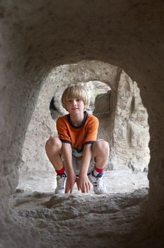 smiling boy sitting behind the stone tunnel