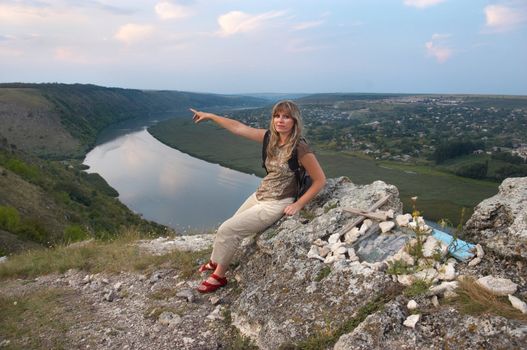 Hiking blond are resting on top of hill near the Dnieser river in Tsipova, Moldova. She is showing onto something with her hand.
