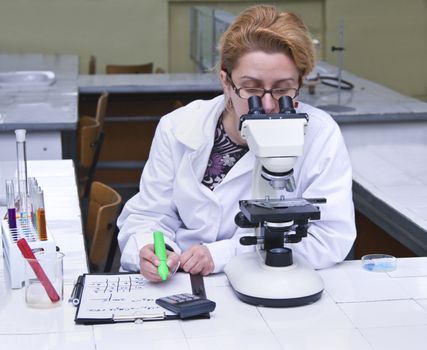 Female researcher taking notices while she is using a microscope.All inscriptions are mine.