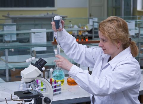 Image of a female researcher dropping a solution into a recipient in a laboratory.