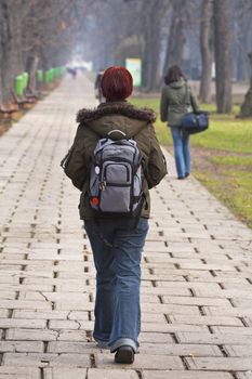 Redhead teen with backpack walking in an autumn park.