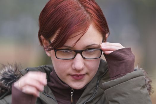 Redheaded girl putting on her glasses outdoors in an autumn park.Motion blur on her right hand.