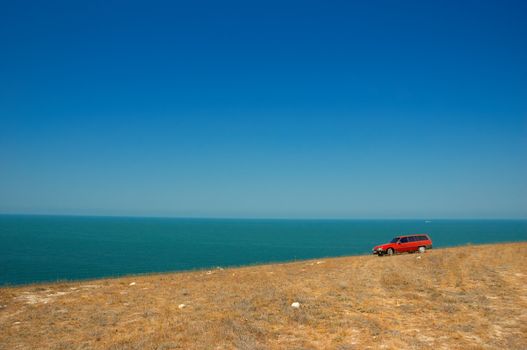 red car on the slope on the sky and sea background