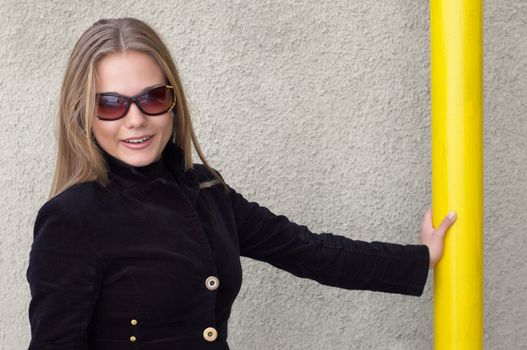 cute girl in black with sunglasses staying near the wall