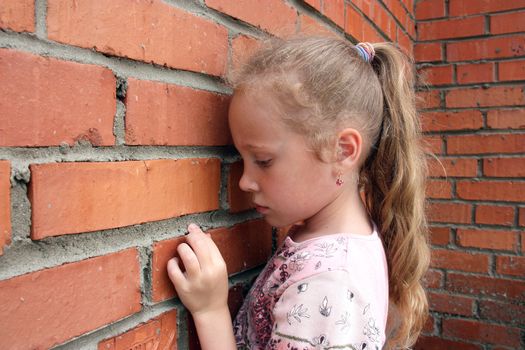 sad little girl standing in front of a brick wall