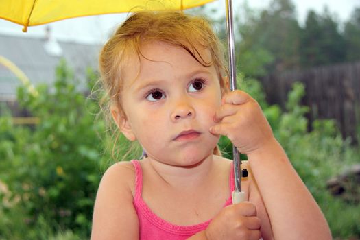 thoughtful little girl standing in the rain holding an umbrella.