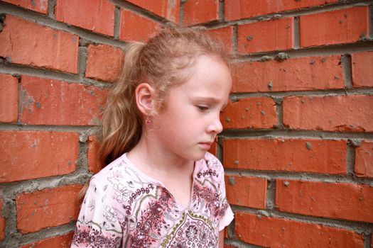 sad little girl standing in front of a brick wall