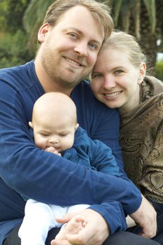 Beautiful happy family of three sitting in the garden laughing. Focus is on the mother