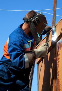 A welder working at height on a background of blue sky