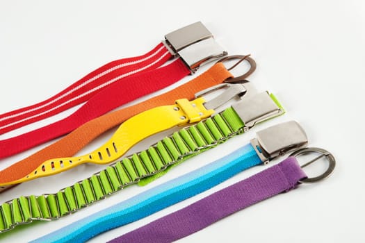 Seven textile belts with metal buckles over the bright background
