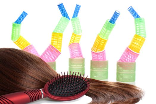 Dark brown and long female hair, red comb and colorful hair curlers at the background. Isolated over white