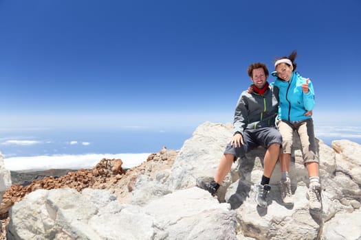 Couple on mountain top of volcano Mount Teide, Tenerife after hiking to summit. Woman showing thumbs up success sign.