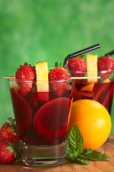 Two glasses of refreshing red wine punch called sangria mixed with orange, apple and mango, garnished with strawberries and pineapple on skewer surrounded by fruits (Selective Focus, Focus on the fruits on the skewer of the first drink)