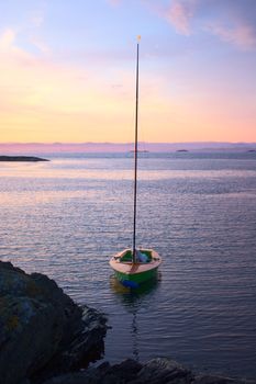 Small sailing boat anchoring at a small rocky island along the Norwegian coast close to Stavanger at sunrise 