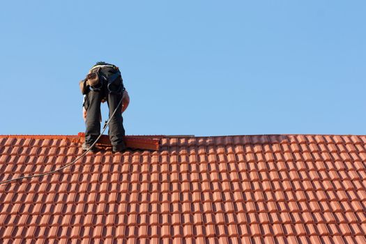 Roofer finishing laying the tiles on the roof of a building