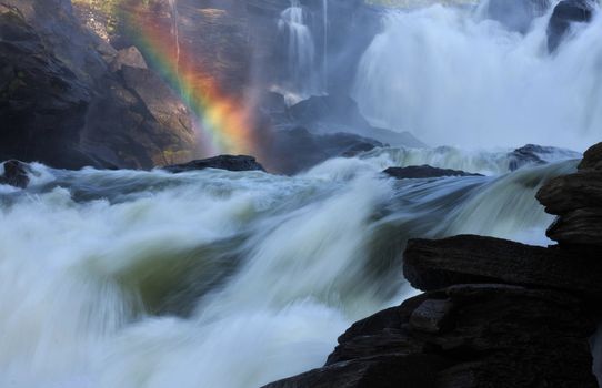 Raging river creates rainbow when steam meets sunlight.