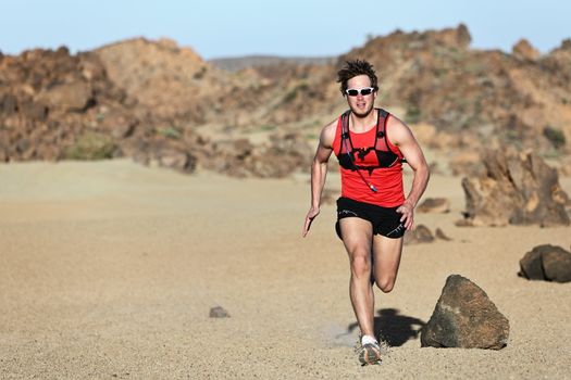 Male runner running / sprinting fast during adventure marathon run in beautiful desert landscape. Strong fit muscular fitness sport man model.