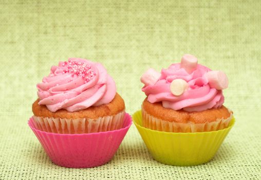 Fresh vanilla cupcakes in pink cup with strawberry icing on decorative background