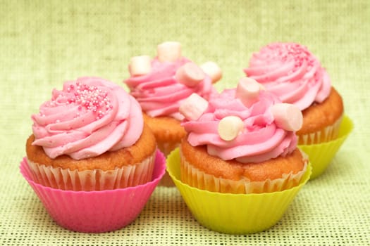 Fresh vanilla cupcakes in pink cups with strawberry icing and marshmallows on decorative background