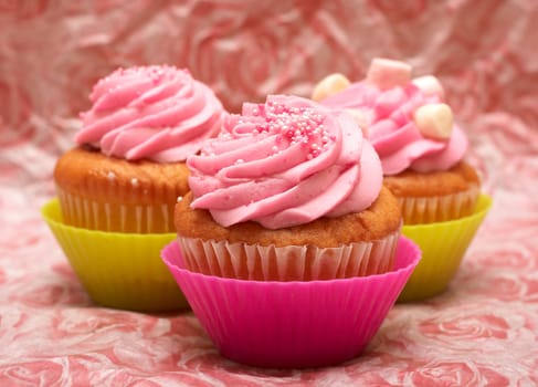 Fresh vanilla cupcakes in pink cups with strawberry icing and marshmallows on decorative background