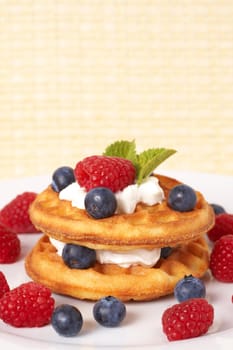 Belgian waffles with fresh raspberries, blueberries, mint leaves and cream on white plate