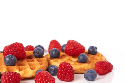 Belgian waffles with fresh raspberries and blueberries on white plate