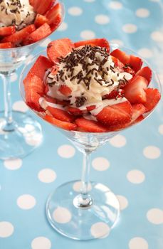 Sliced fresh strawberries with cream and chocolate decoration in martini glasses on blue polka dot background