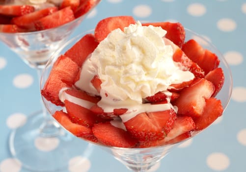 Sliced fresh strawberries with cream in martini glasses on blue polka dot background