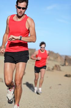 Running sport. Man runner looking at heart rate monitor watch during adventure marathon run in beautiful desert landscape.